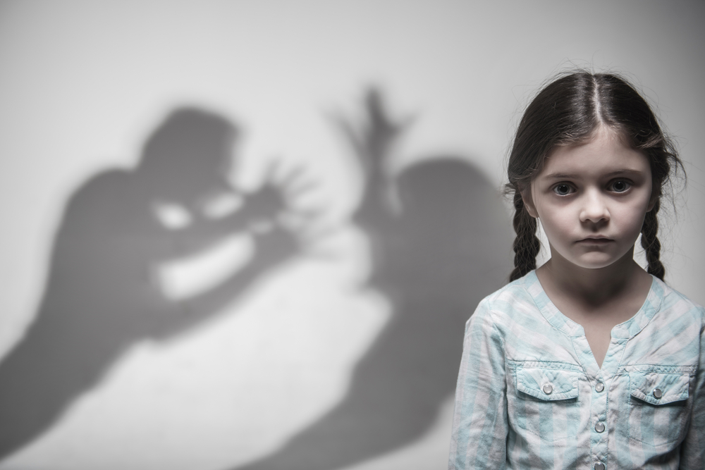 shadows of parents arguing behind a sad little girl