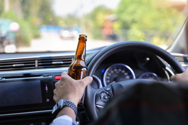 driver behind wheel with beer bottle in hand