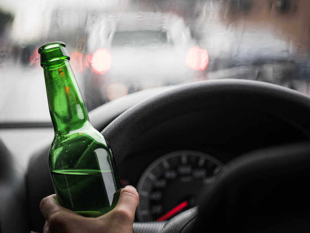 man driving car with beer bottle in hand