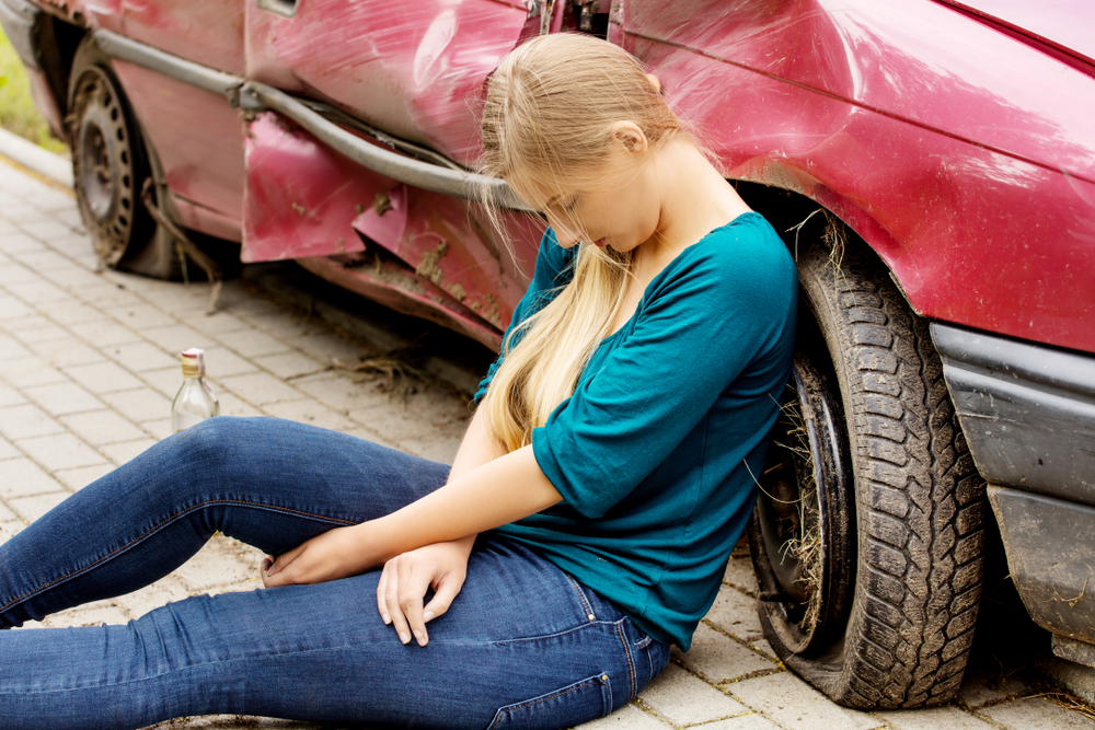 An intoxicated teen sitting in front of her damaged vehicle after a collision will need a Rowlett underage DWI lawyer to navigate potential penalties and legal defenses.
