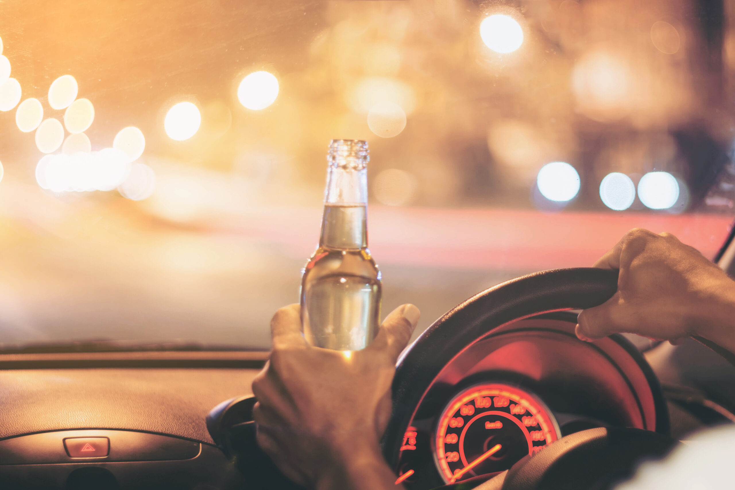A drunk motorist is holding an open alcohol bottle while operating a car. The help of a Desoto DUI attorney is necessary to mitigate legal consequences.